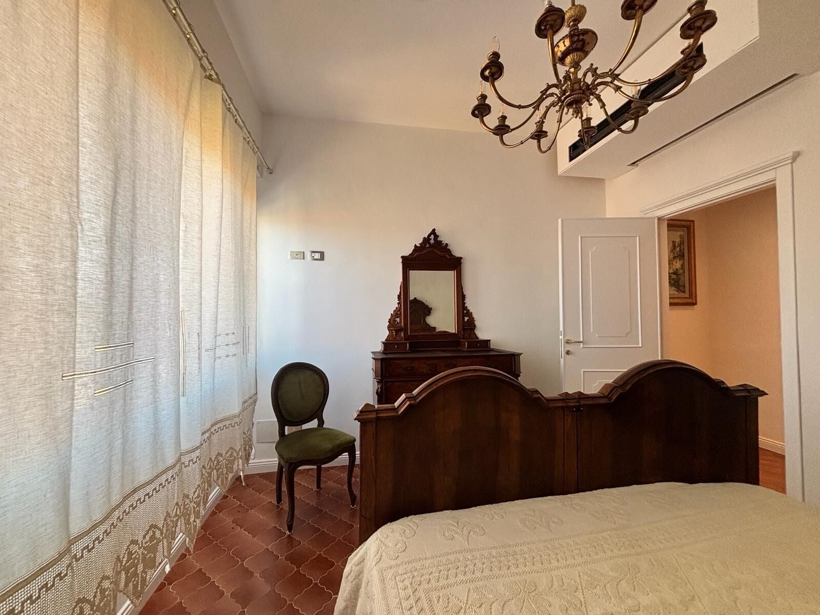 Un dormitorio con cama, cómoda de madera, silla, candelabro y puerta.