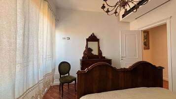 Un dormitorio con cama, cómoda de madera, silla, candelabro y puerta.