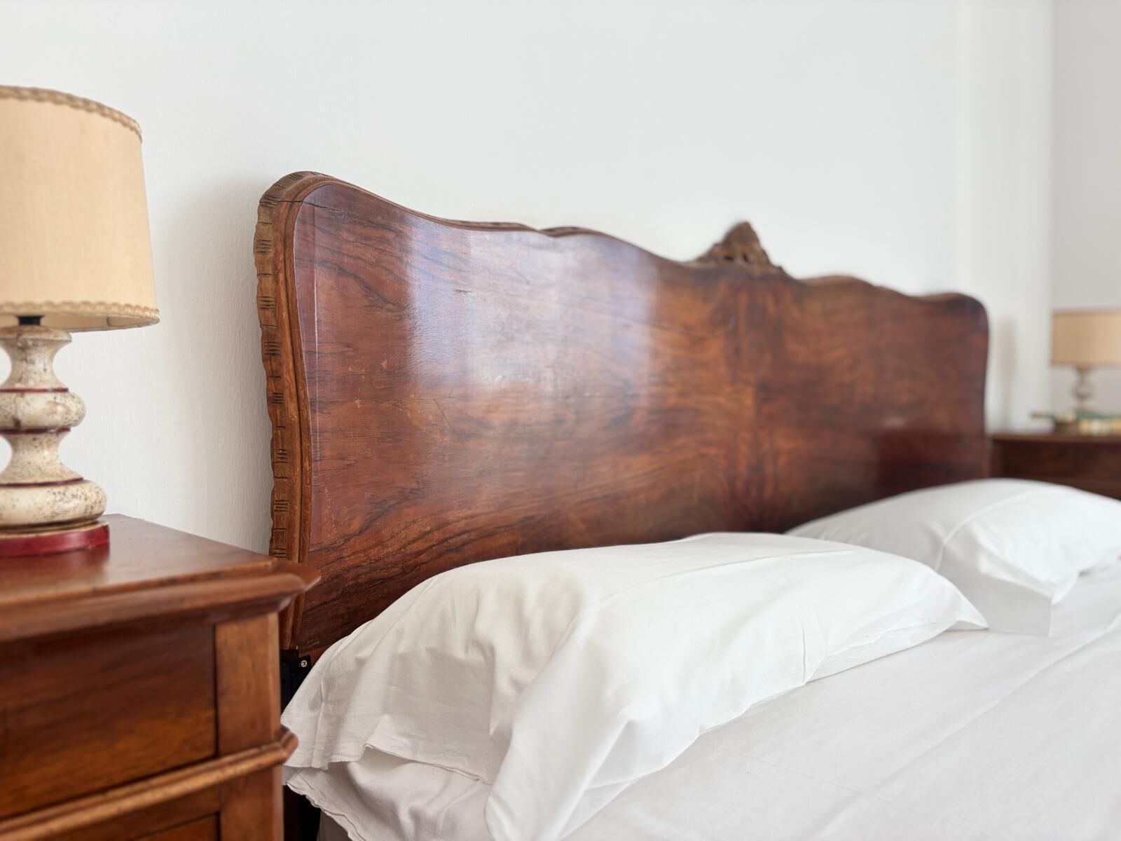 Une tête de lit en bois, un couvre-lit blanc et une table de chevet avec une lampe.