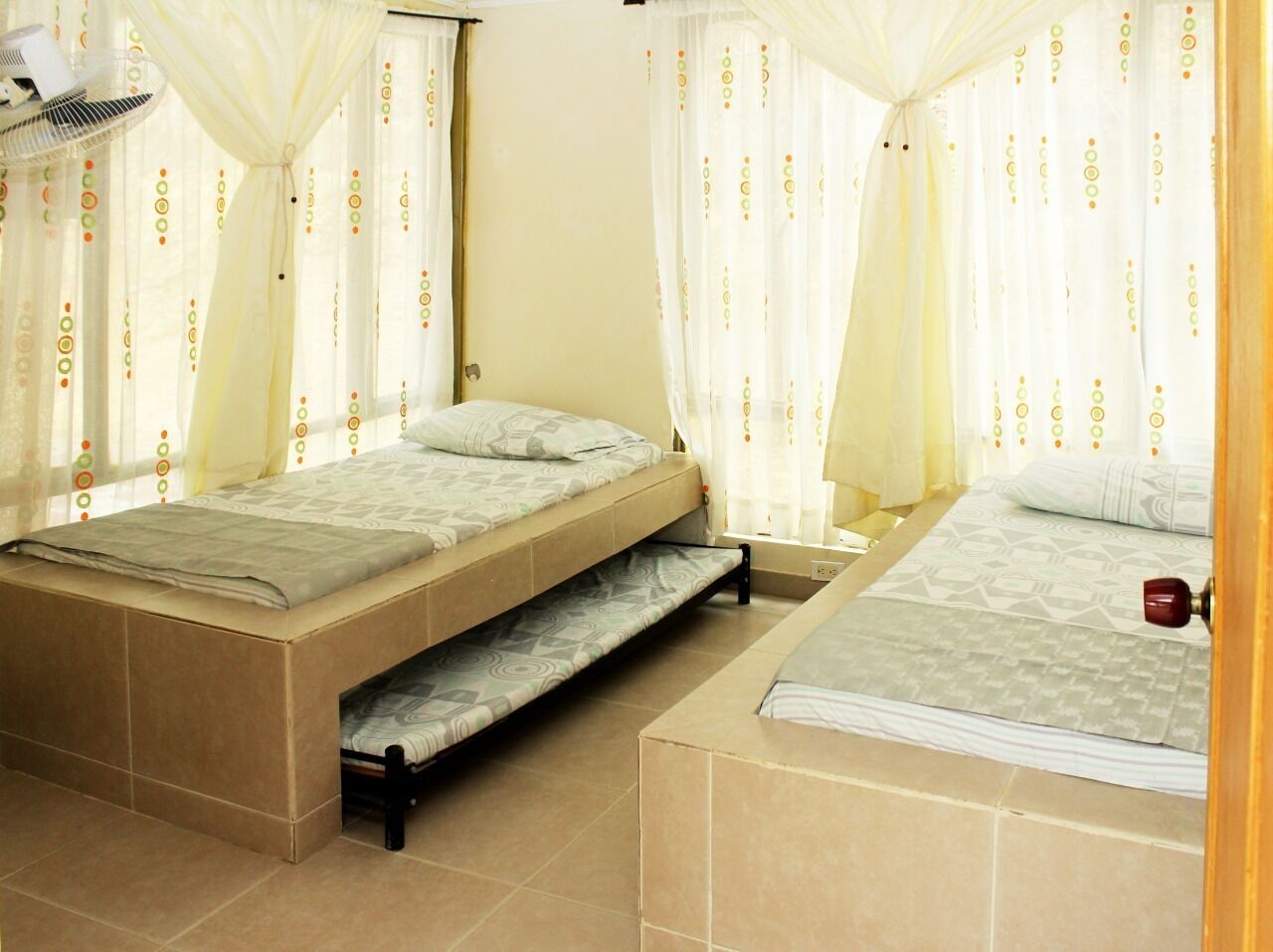 A bedroom with two beds, a ceiling fan, and curtains with a circular pattern.
