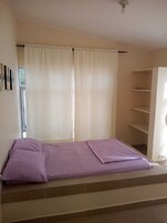 Una habitación con cama, ventana con cortinas, pared con estante y ventilador de techo.
