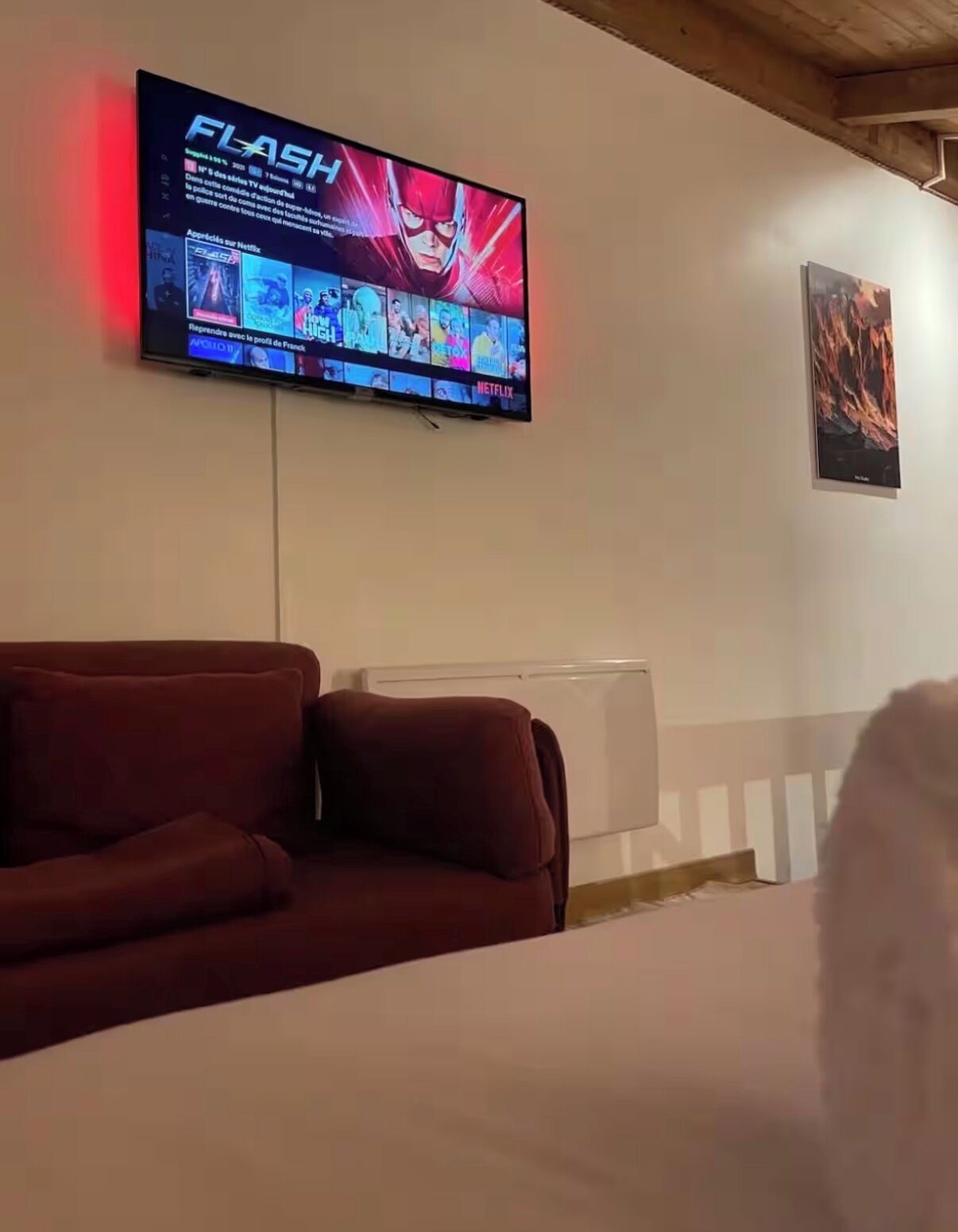 A TV mounted on a wall displaying a streaming service interface, a red sofa, and a radiator below.