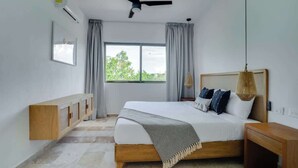 Una camera da letto con un letto, una ventola a soffitto, una finestra con tende, un comodino e un tavolino.