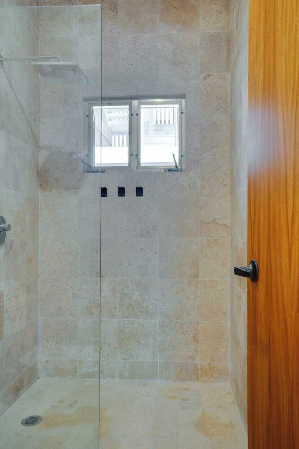 Une douche avec une porte en verre, une fenêtre et une porte en bois.