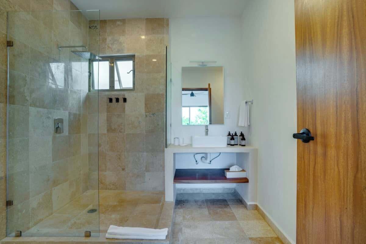 Une salle de bain moderne avec une douche à parois de verre, un lavabo blanc avec un miroir au-dessus et une porte en bois.