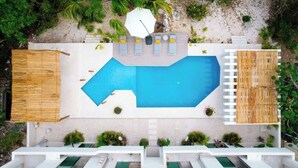 En pool på taket med solstolar, ett litet parasoll och ett trädäck.