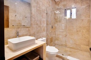 Een moderne badkamer met een groot rechthoekig wastafelmeubel, een toilet en een douchecabine met glazen wanden.