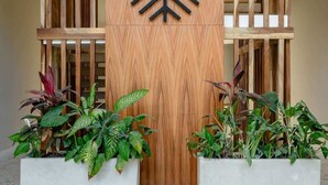 A wooden reception desk with a logo, two planter boxes with plants, and a tiled floor. - Casa Manglar - Golf Course Views, Near the Ocean (Puerto Aventuras)