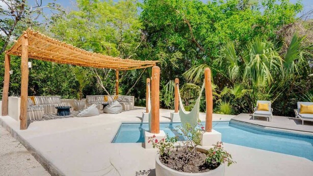 A pool area with a pergola, lounge chairs, and a planter with plants. - Casa Manglar - Golf Course Views, Near the Ocean (Puerto Aventuras)