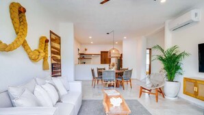 A modern living room with a white sofa, a wooden coffee table, and a dining area with a chandelier. - Casa Manglar - Golf Course Views, Near the Ocean (Puerto Aventuras)