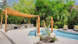 Et poolområde med en pergola, liggestole og en plantekasse med planter.