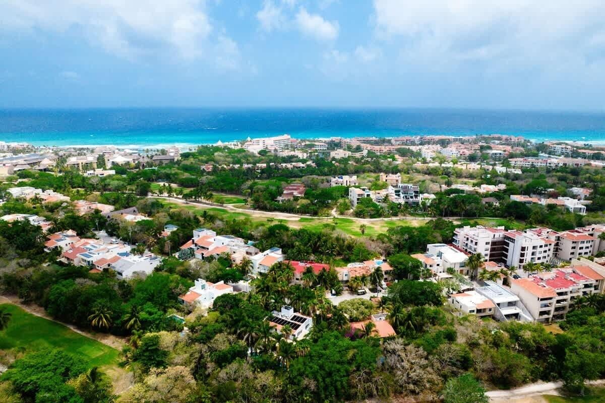 An aerial view of a coastal residential area with houses, greenery, and a clear view of the ocean.