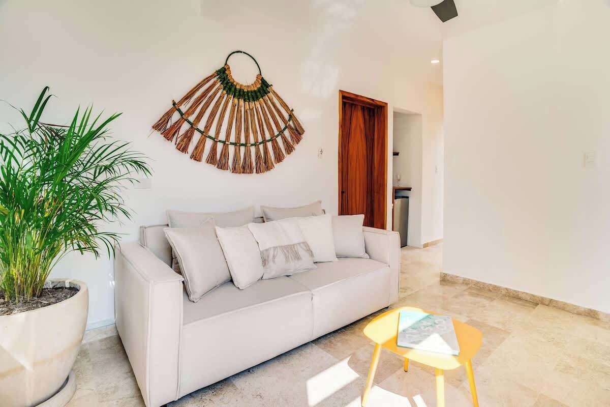 A modern living room with a sofa, a small table, a potted plant, and a wall hanging.