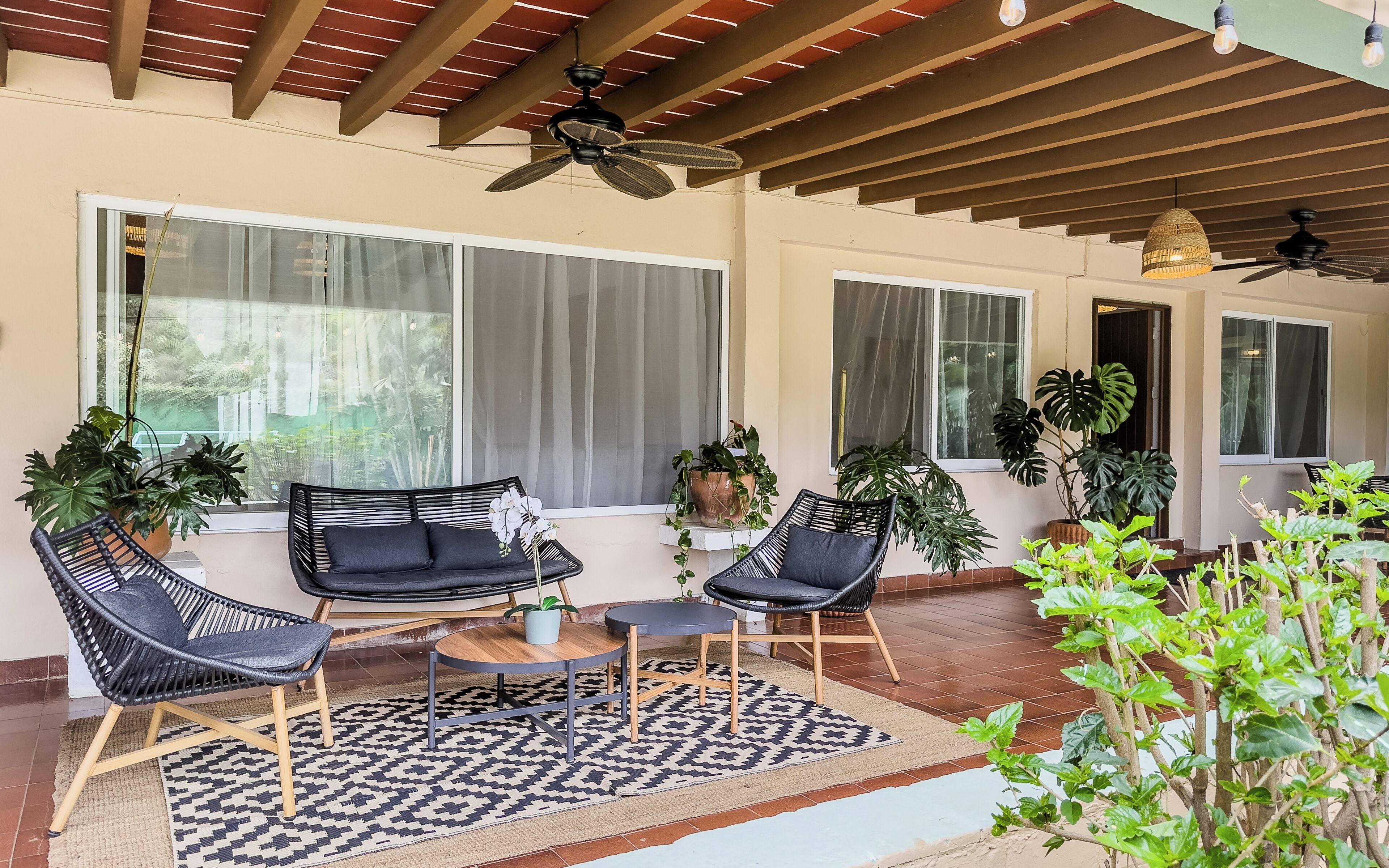 A covered patio with outdoor furniture, ceiling fans, and potted plants.
