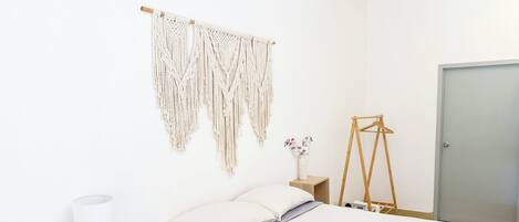 A minimalist bedroom with a bed, bedside tables, a macrame wall hanging, and a wooden hanger.