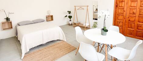 Un dormitorio con cama, mesitas de noche, una silla colgante, una pequeña mesa con sillas y una puerta de madera.