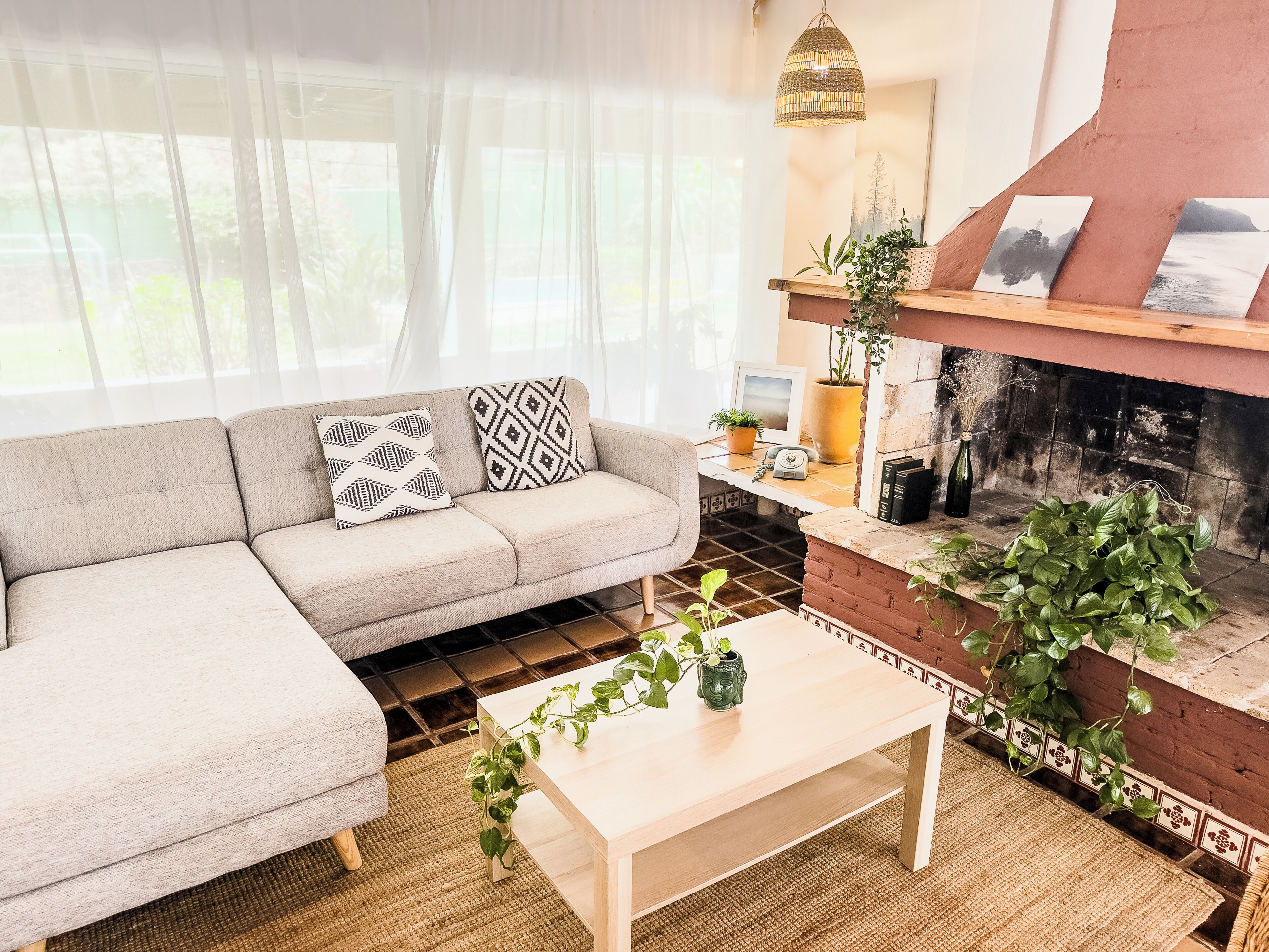 A living room with a sofa, a coffee table, a fireplace, and a window with sheer curtains.