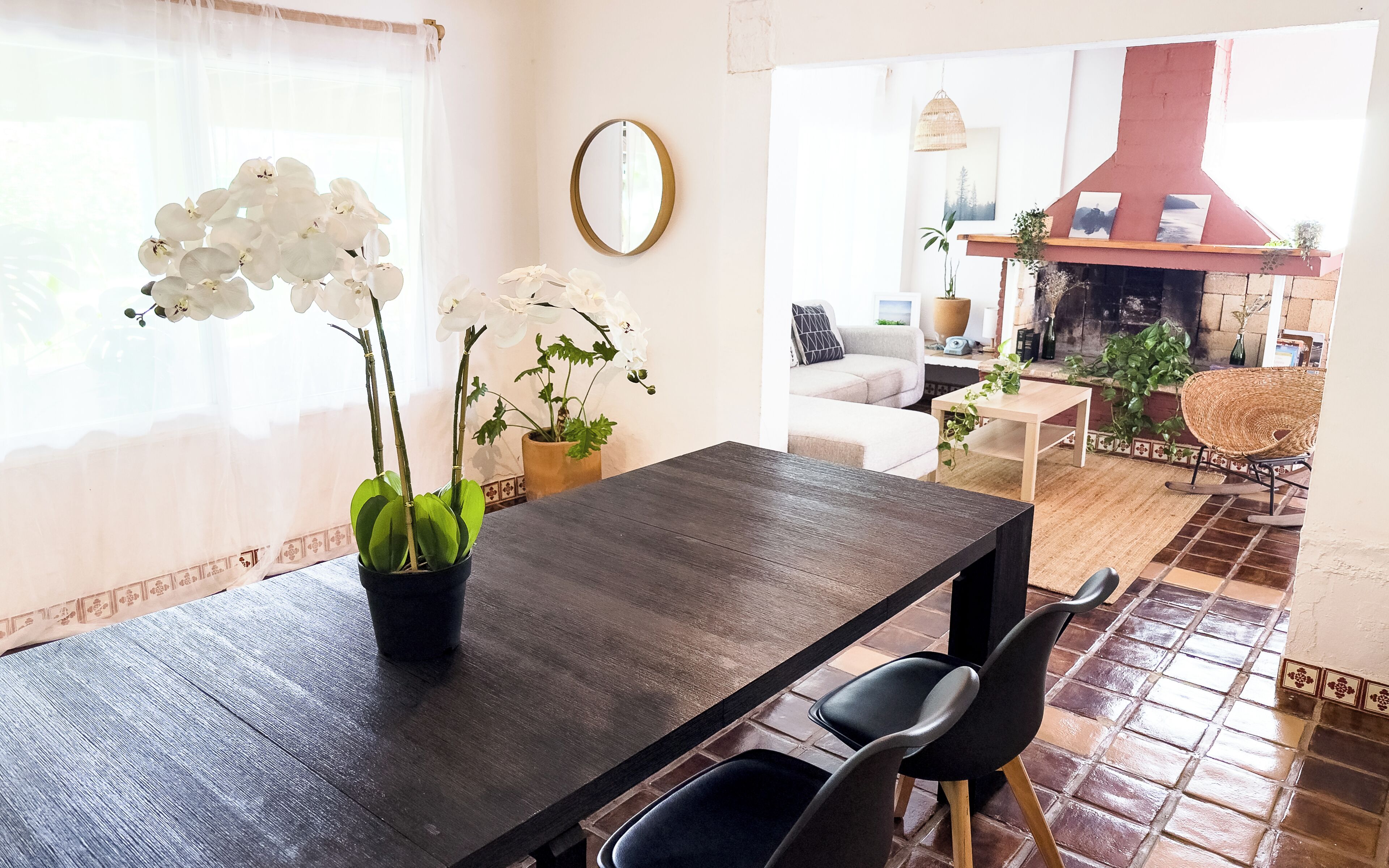 Un comedor con una mesa de madera oscura, dos sillas y orquídeas blancas en una maceta negra.