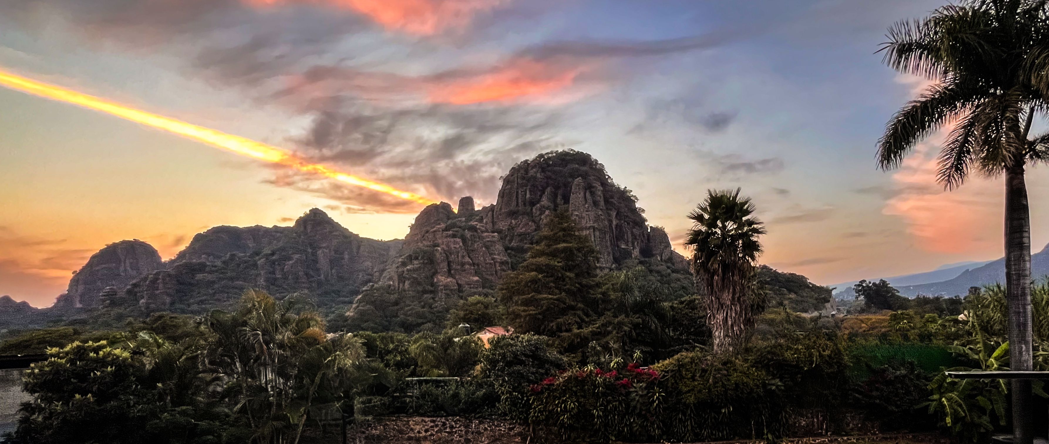 A mountainous landscape with a sunset, palm trees, and dense vegetation.