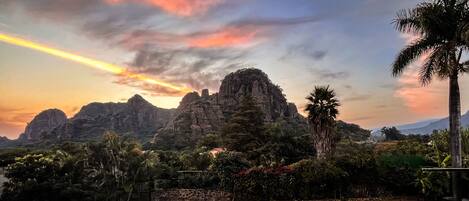 A mountainous landscape with a sunset, palm trees, and dense vegetation.