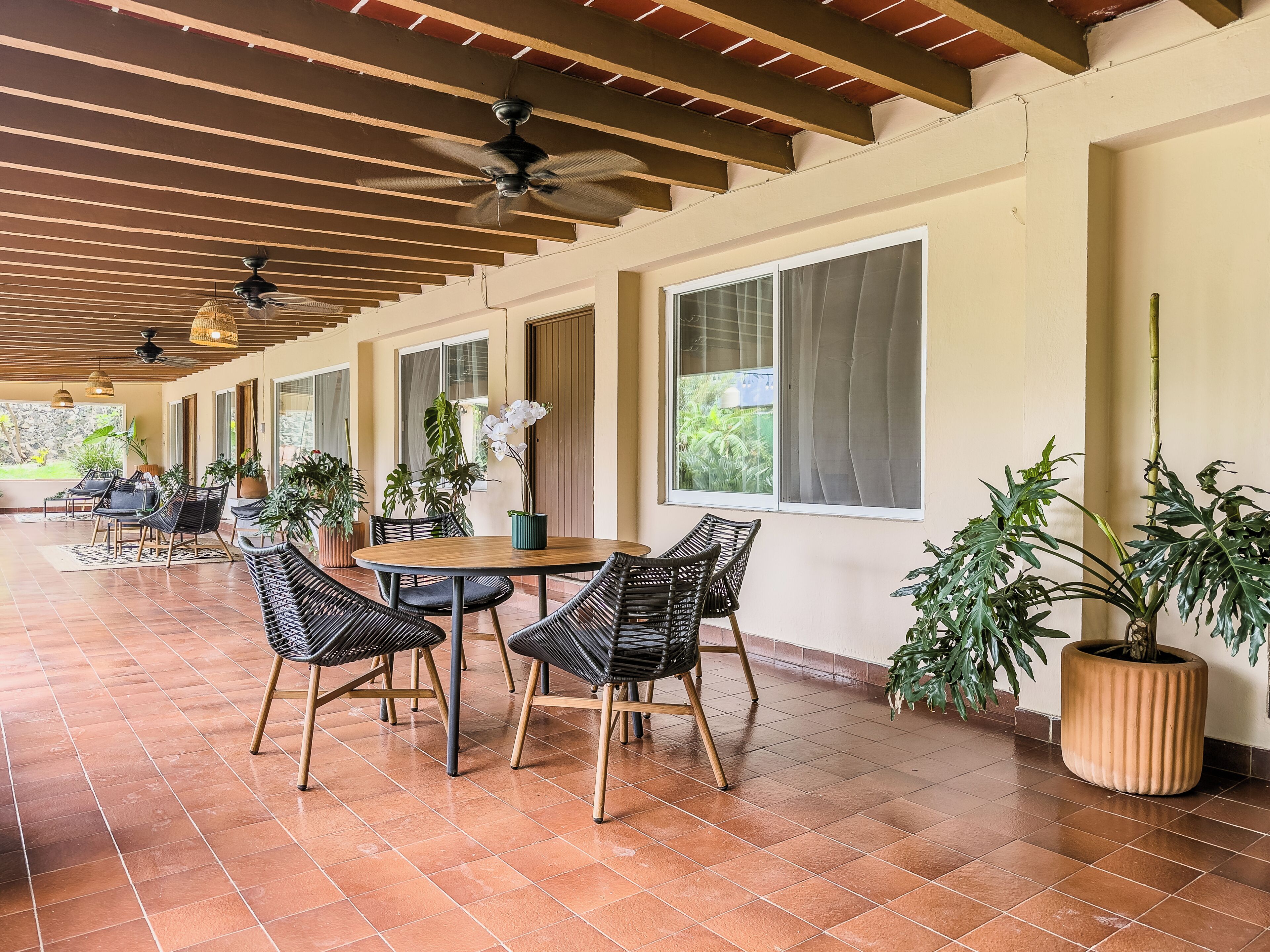 Un patio techado con una mesa redonda y sillas, plantas en macetas y un ventilador de techo.