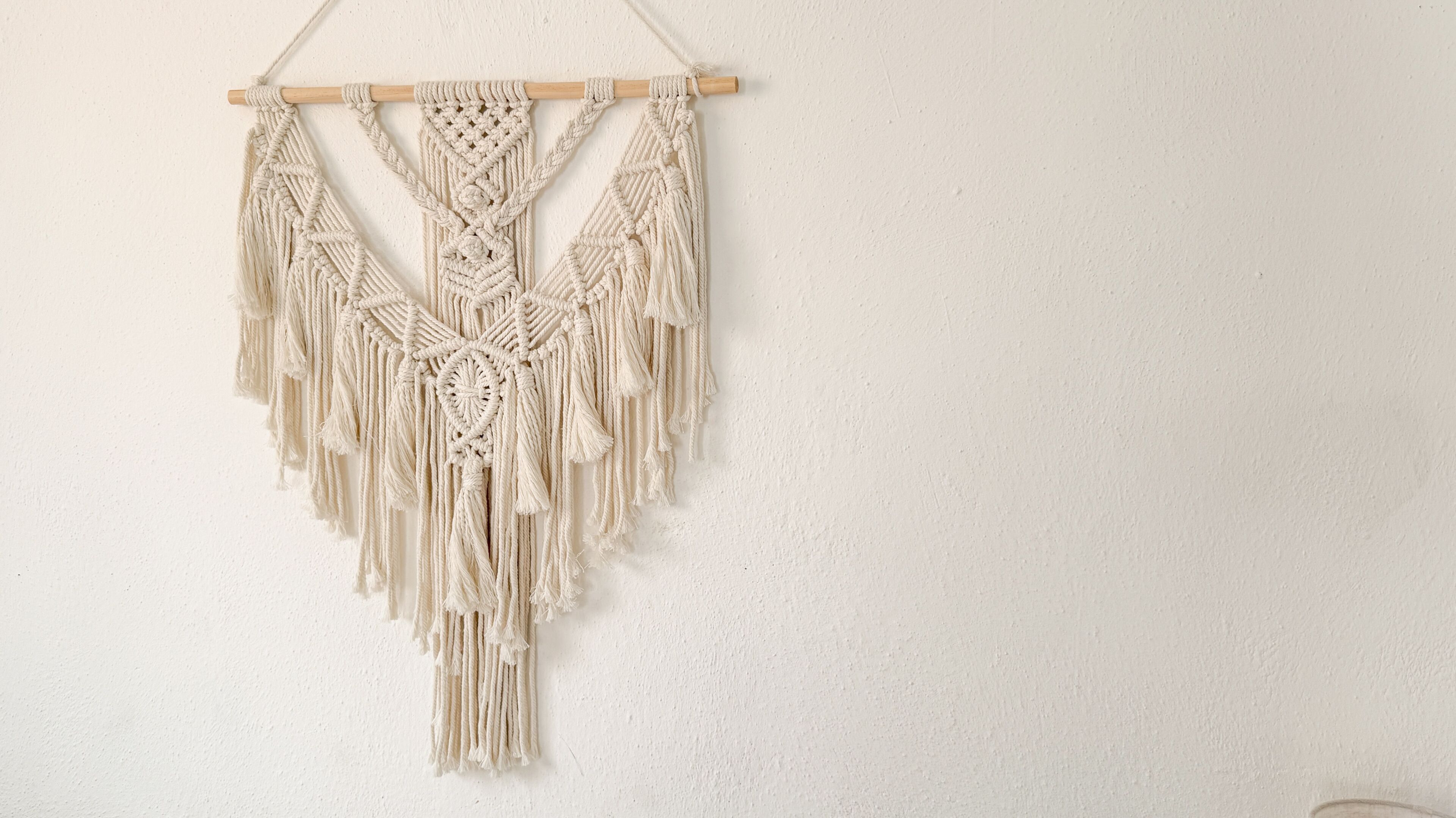 Un tapiz de macramé con marco de madera, con elaborados diseños de nudos y flecos.