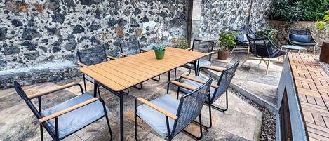 Un patio con mesa y sillas de madera, rodeado por un muro de piedra y macetas con plantas.