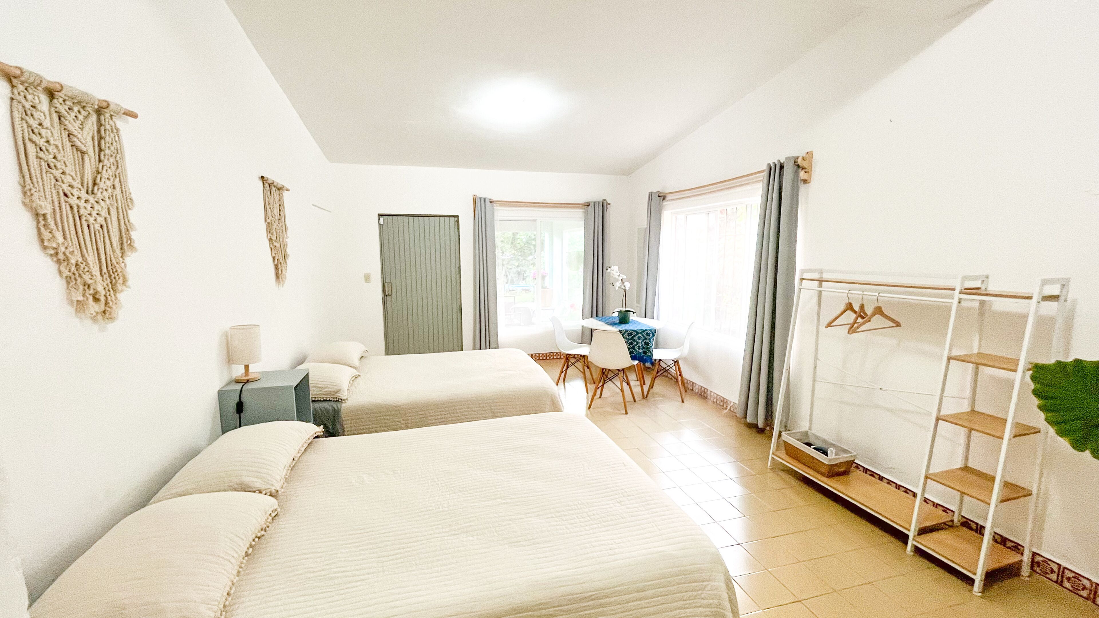 A room with two beds, a desk with chairs, a hanging clothes rack, and a door.