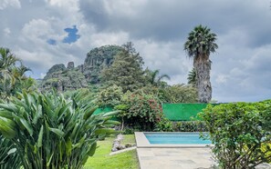 Una piscina rodeada de exuberante vegetación y con una montaña al fondo.