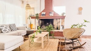 A living room with a sofa, a coffee table, a wicker chair, a fireplace, and a tiled floor.