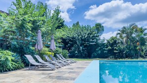 A pool area with lounge chairs and umbrellas, surrounded by lush greenery.