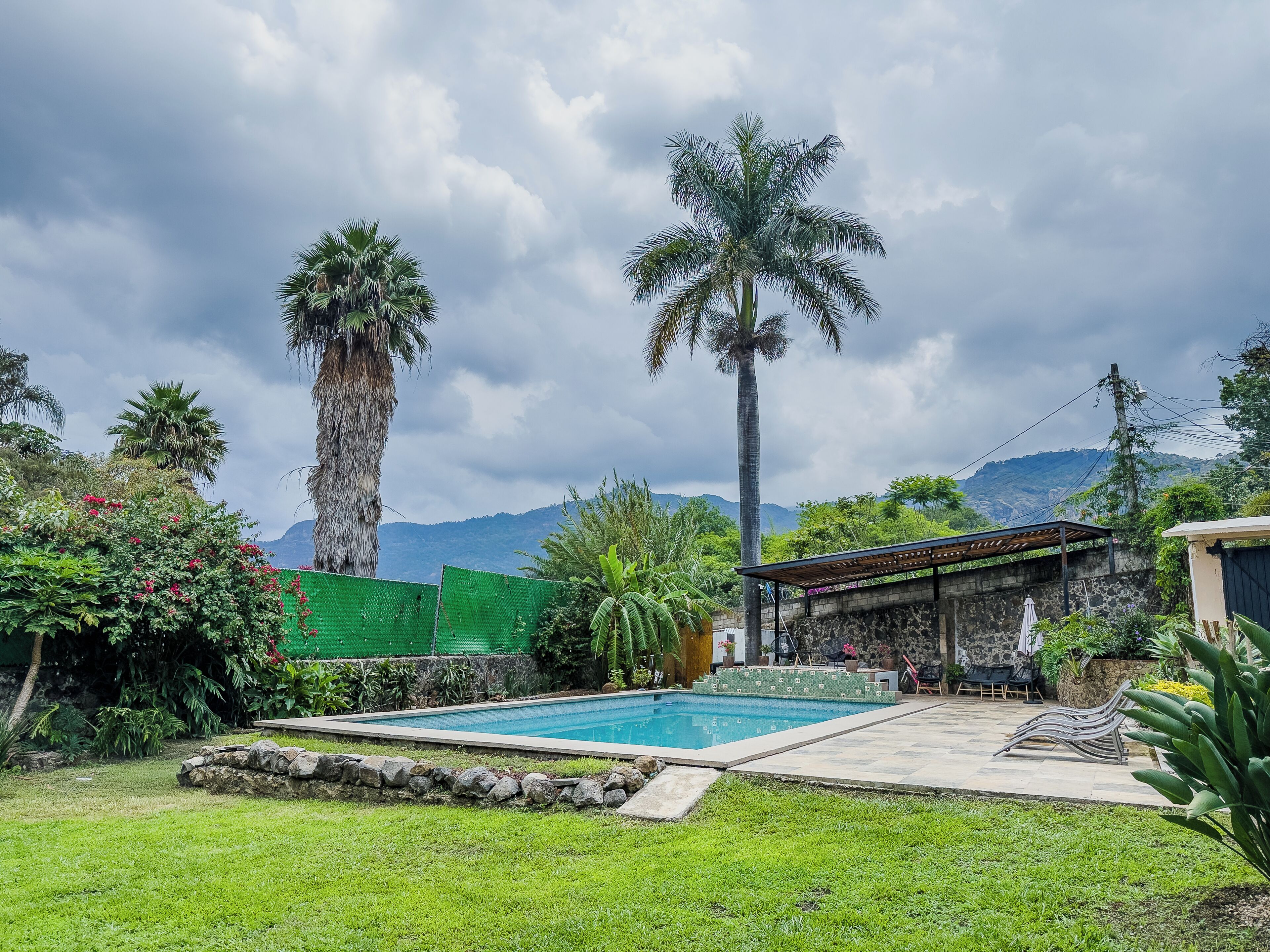 Una piscina con borde de piedra, rodeada de césped y plantas, con vistas a montañas al fondo.