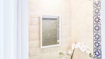 Un baño con pared de azulejos, un lavabo, un espejo y una planta en maceta.