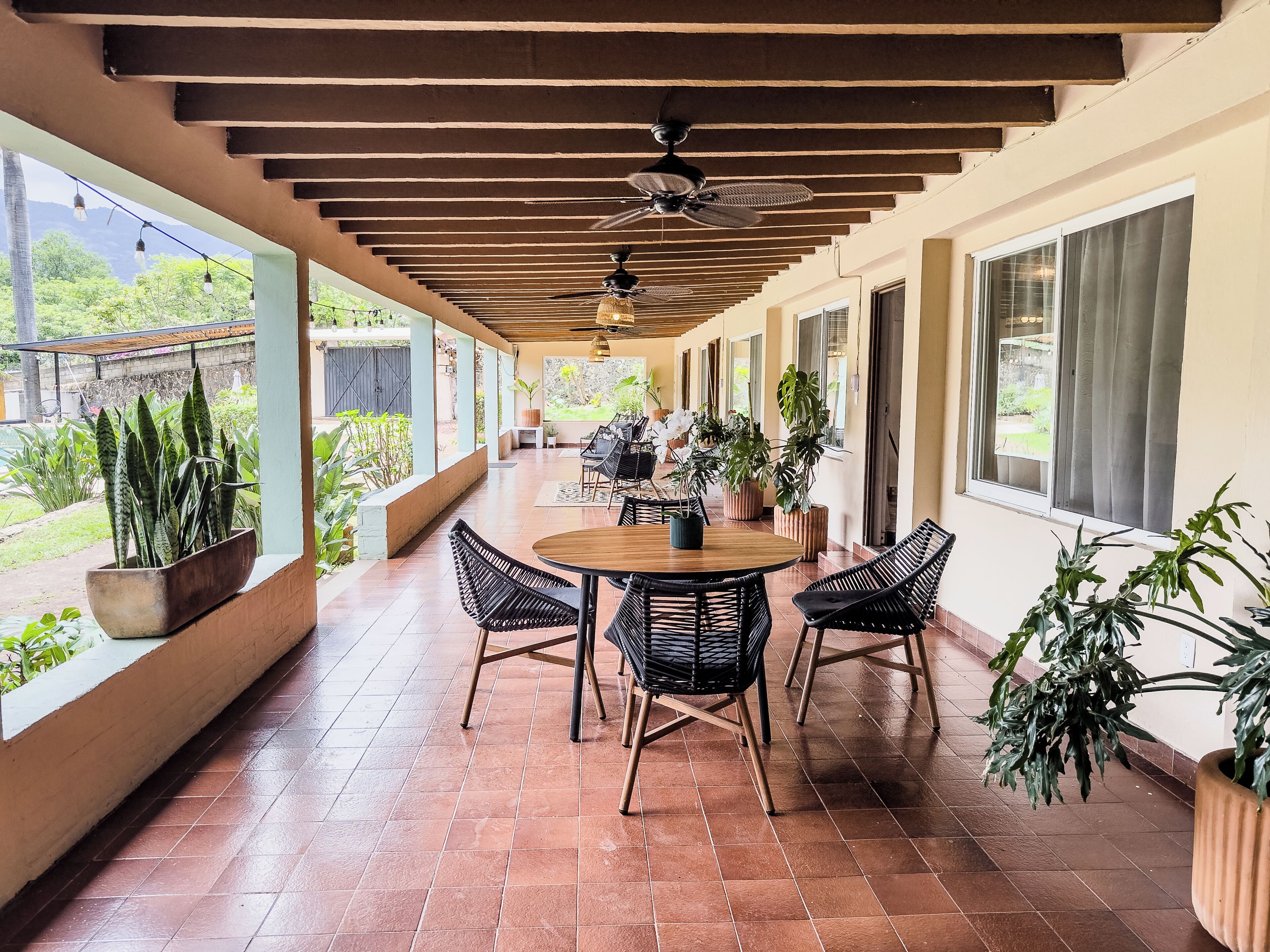 A covered patio with a round table, chairs, ceiling fans, and potted plants.