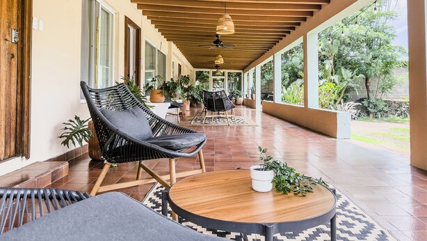 A covered outdoor seating area with wicker chairs, a round wooden table, and potted plants.