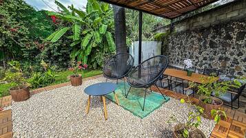 Un patio al aire libre con una mesa y sillas, rodeado de plantas en macetas y un muro de piedra.