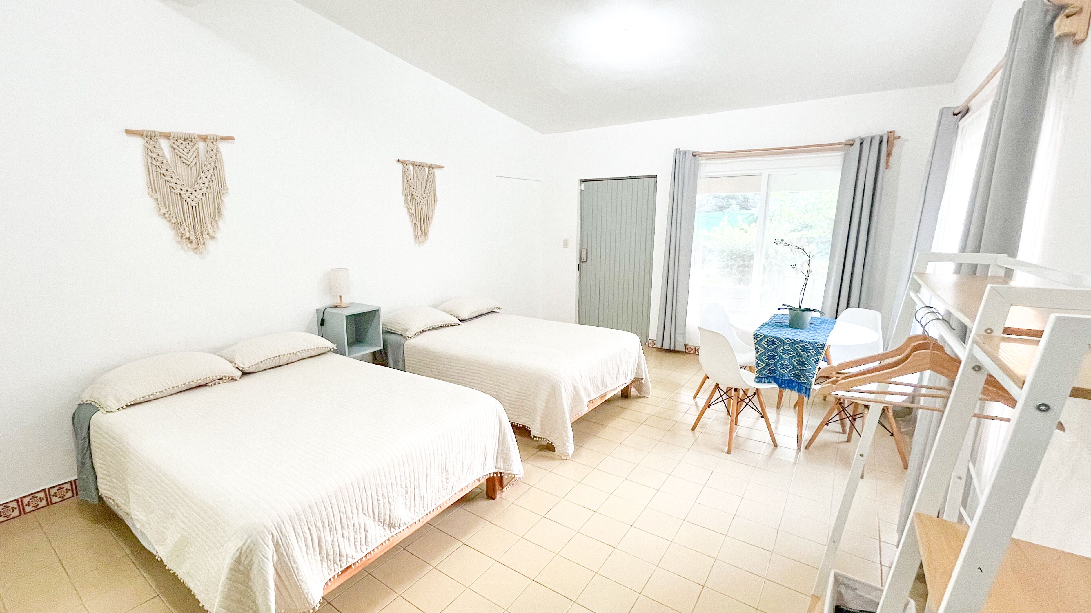 Hotellihuone, jossa on kaksi sänkyä, työpöytä tuolilla, pieni pöytä, jossa on kasvi, ja vaatekaappi.