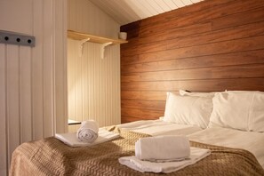 Ein Hotelzimmer mit einem hölzernen Kopfteil, einem Bett mit weißen Leinentüchern und einem zusammengerollten Handtuch auf dem Bett.