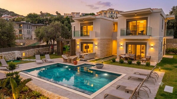 A modern two-story house with a swimming pool, outdoor seating, and a view of the surrounding neighborhood.