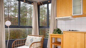 Een kamer met een houten stoel, een klein tafeltje, een kast en een raam met uitzicht op bomen.