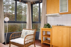 A room with a wooden chair, a small table, a cabinet, and a window with a view of trees.