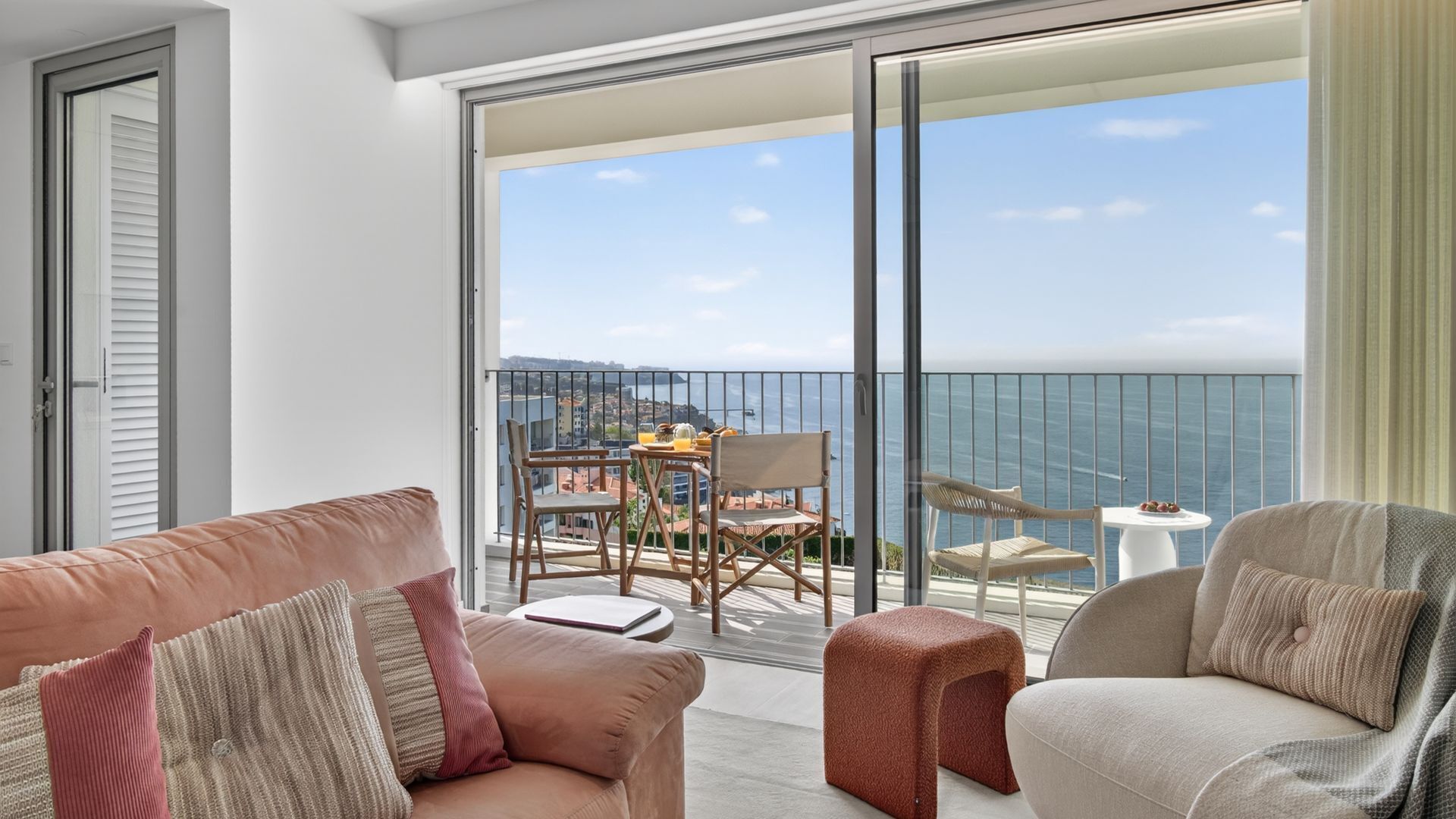 A balcony with a view of the sea, furnished with a sofa, chairs, and a small table.