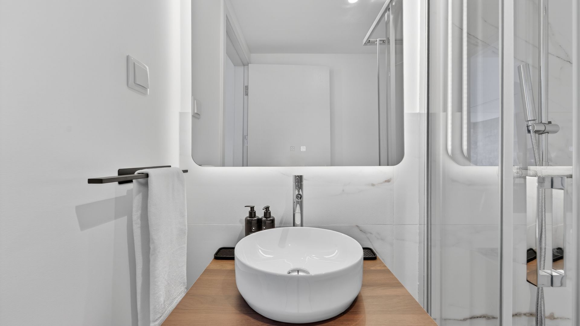 Une salle de bain moderne avec un grand miroir, un lavabo sur colonne et une douche à parois de verre.
