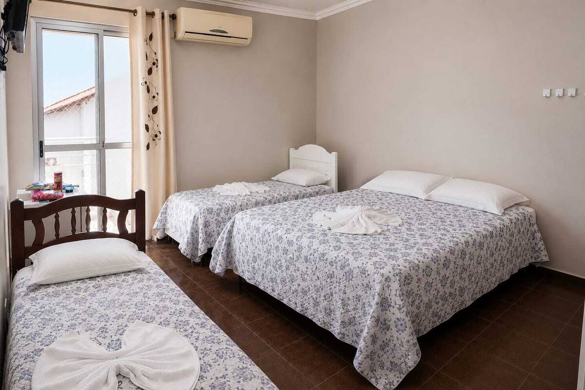Une chambre d’hôtel avec deux lits, une fenêtre avec des rideaux, un appareil de climatisation et une petite table sur laquelle se trouvent divers objets.