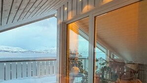 Eine Holzterrasse mit Blick auf verschneite Berge, eine Glastür und ein Stuhl.