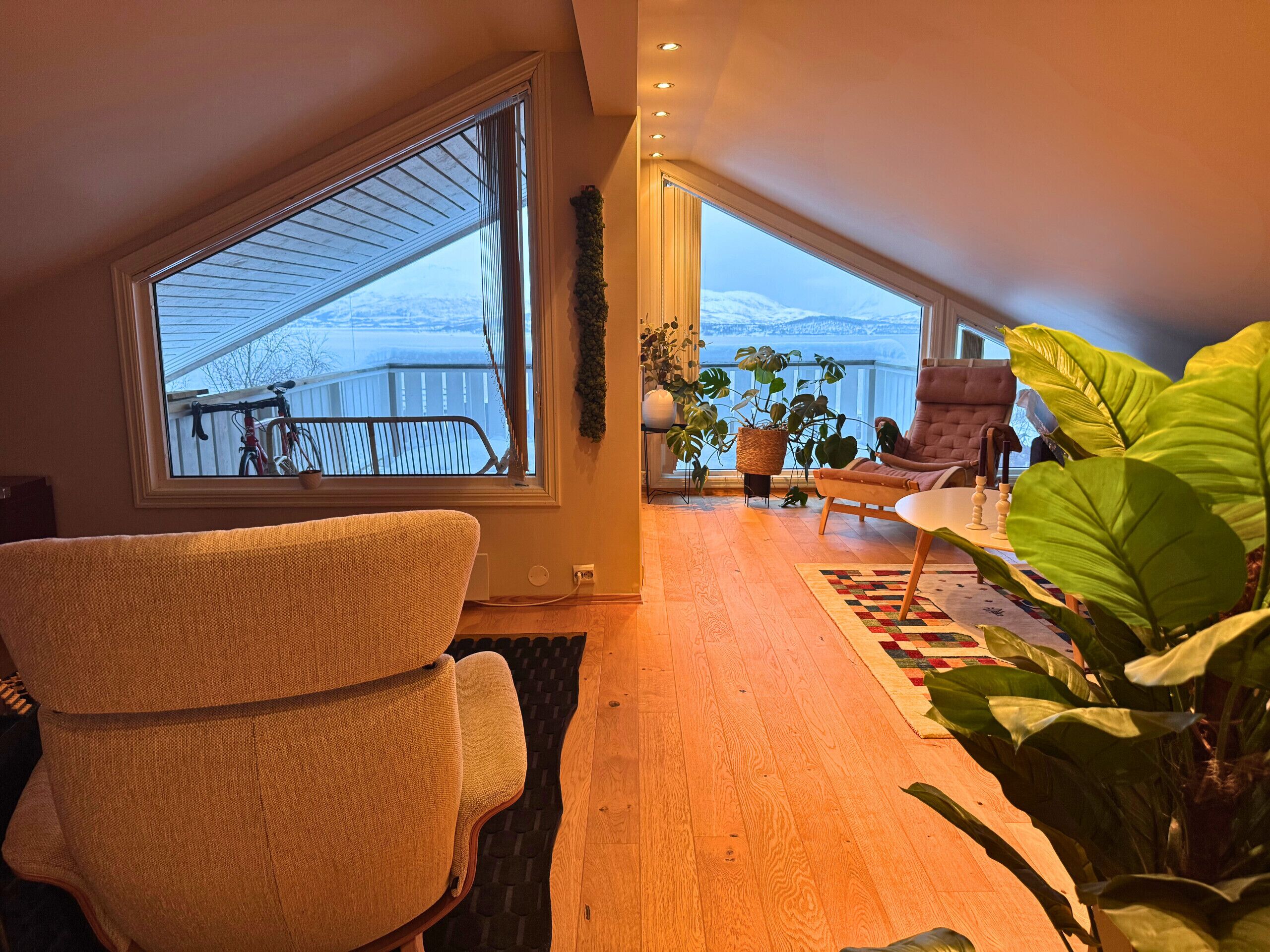 A spacious loft with a large skylight, a cozy seating area with a chair and a table, and a view of a snowy landscape.