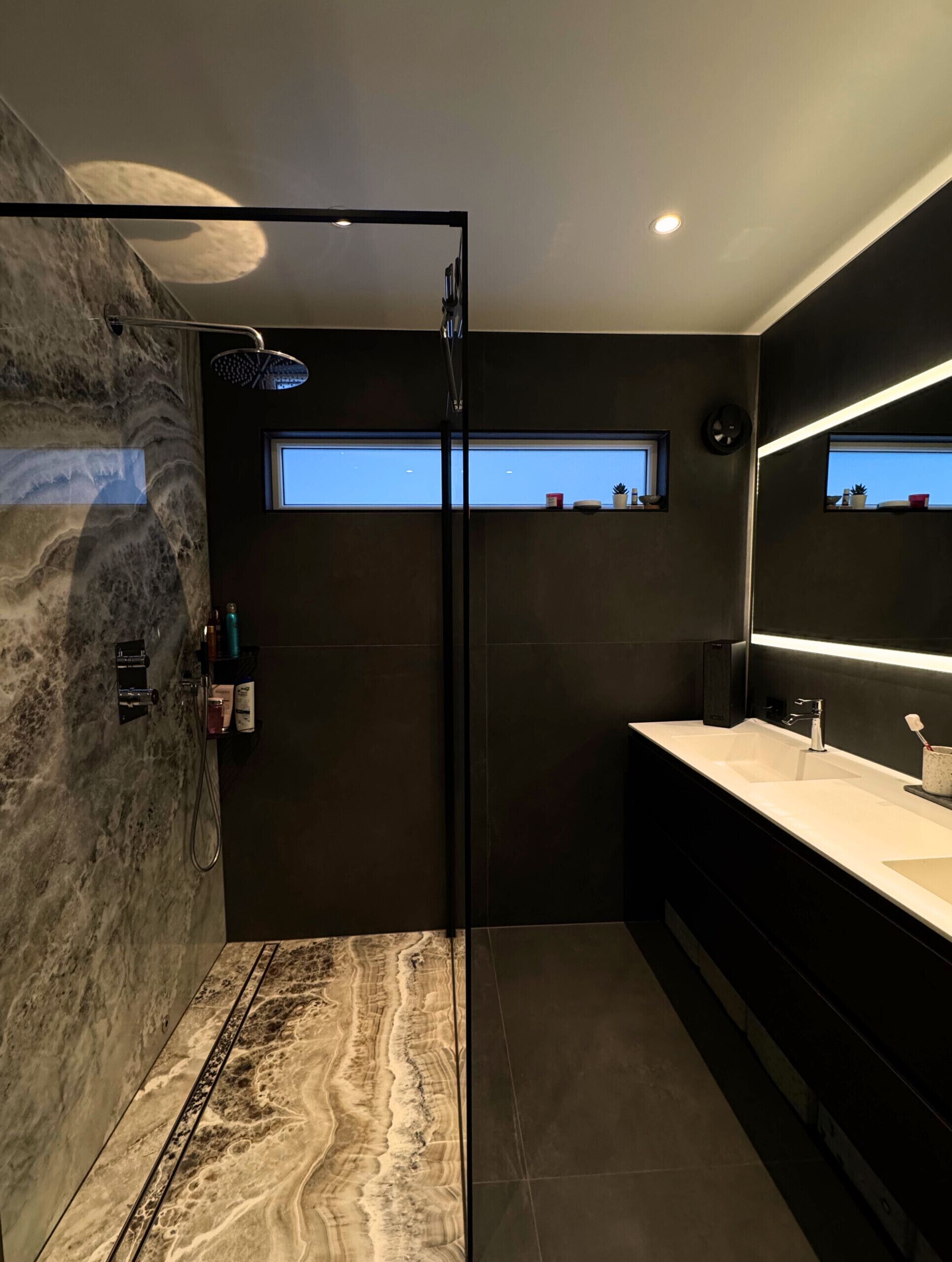 A modern bathroom with a marble shower, a large mirror, and a vanity with a sink.