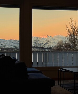 Una habitación con un amplio ventanal que da a un paisaje montañoso nevado al atardecer.