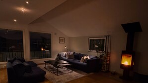 Ein modernes Wohnzimmer mit einer Couch, Couchtisch, Kamin und großen Fenstern.