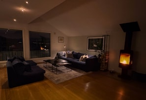 Ein modernes Wohnzimmer mit einer Couch, Couchtisch, Kamin und großen Fenstern.